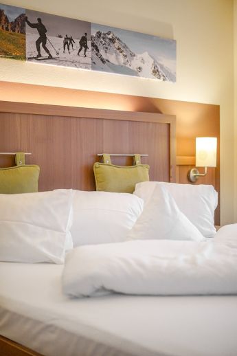 Ein Doppelbettzimmer im Hotel Lärchenhof mit Bildern von Bergwanderungen über dem Bett