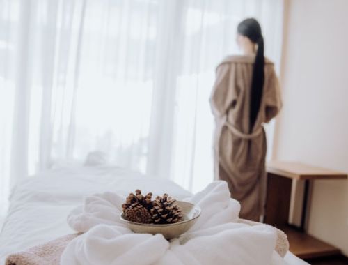 Eine ruhige Spa-Umgebung mit einer Frau im Bademantel, einer Schale mit Tannenzapfen und weichen Handtüchern, bereit für eine Massage im Hotel Lärchenhof