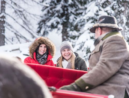 Zwei Frauen in warmer Winterkleidung genießen eine Pferdeschlittenfahrt durch die verschneite Landschaft