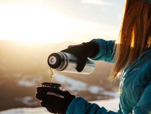 Eine Person gießt sich Tee aus einer Thermoskanne während einer Pause nach einer Skitour, mit Blick auf die winterliche Berglandschaft am Katschberg