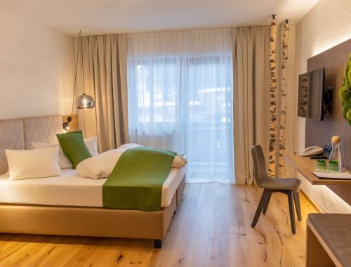 Ein modern gestaltetes Zimmer im Hotel Lärchenhof, mit einem großen Wandbild von einem Wald und gemütlichen Sitzgelegenheiten