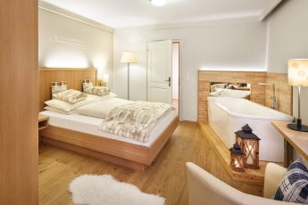 Ein gemütliches Hotelzimmer mit einem großen Bett, einer Badewanne und einer warmen Beleuchtung, perfekt für entspannte Nächte im Hotel Lärchenhof