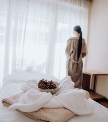 Eine ruhige Spa-Umgebung mit einer Frau im Bademantel, einer Schale mit Tannenzapfen und weichen Handtüchern, bereit für eine Massage im Hotel Lärchenhof