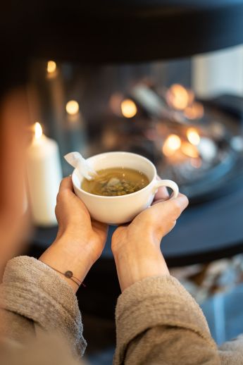 Frau mit Teetasse vor dem offenen Kamin