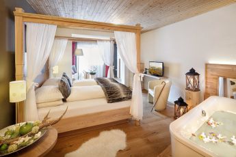 Ein gemütliches Hotelzimmer im Hotel Lärchenhof mit einem großen Bett, einer warmen Holzeinrichtung und einer modernen Badewanne