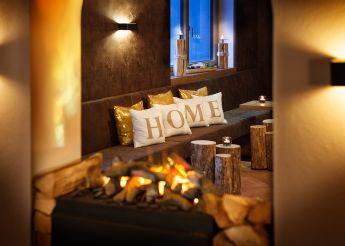 Ein gemütlicher Lounge-Bereich mit Kissen, auf denen "HOME" steht, und einem Kaminfeuer im Hotel Lärchenhof