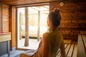 Eine Frau entspannt in einer holzverkleideten Sauna und blickt auf den Außenbereich mit Bäumen
