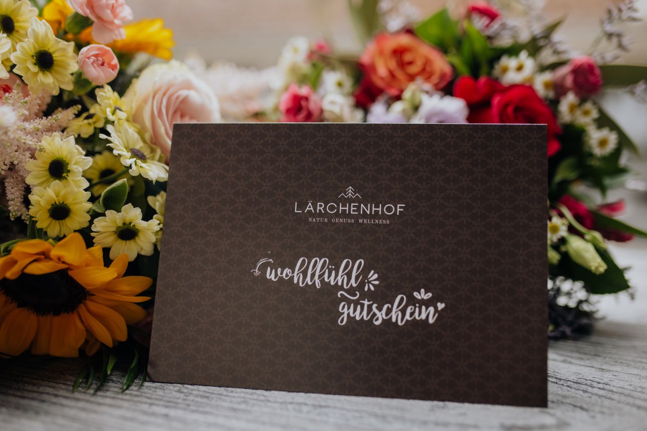 Ein Wohlfühlgutschein des Hotel Lärchenhof umgeben von bunten Blumen